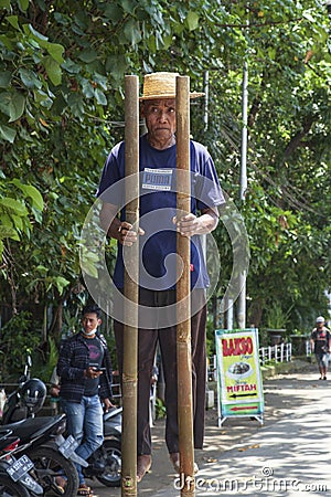 Man walking on stilts along roadside in Denpasar, Bali, Indonesia. Editorial Stock Photo