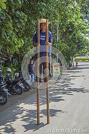 Man walking on stilts along roadside in Denpasar, Bali, Indonesia. Editorial Stock Photo