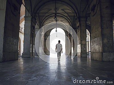 Man walking under heavy vaults, in Pisa, Italy. Bright light seeping in. Stock Photo