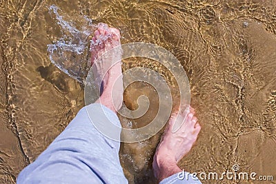 Man is walking on water shallow on sand bottom legs close up summer vacation. Stock Photo