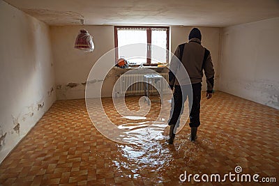 Man walks with rubber boots in a flooded basement room during flood Stock Photo