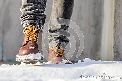 Man walks in the snow street. Feet shod in brown winter boots. Stock Photo