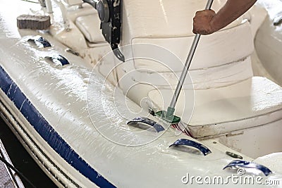 Man washing white inflatable boat with brush and pressure water system at garage. Ship service and seasonal maintenance concept Stock Photo