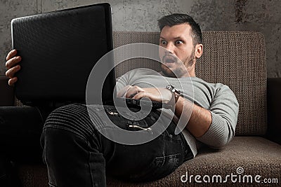 A man watches an adult video on a laptop while sitting on the couch. The concept of porn, masturbation, male needs, pervert, lust Stock Photo