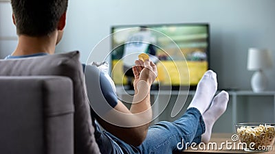 Man watching american football eating snacks on couch home, weekend leisure Stock Photo