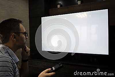 Man watching television, turning on plasma flatscreen TV-set, pointing remote control at empty TV screen. Guy switching channels Stock Photo