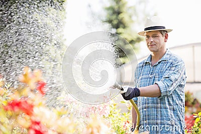 Man watering plants outside greenhouse Stock Photo