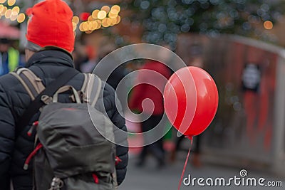 Man wearing backpack and red hat on street with balloon Stock Photo