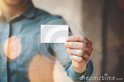 Man wearing blue jeans shirt and showing blank white business card. Blurred background. Horizontal mockup Stock Photo