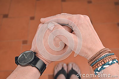 Man wearing a bracelet made of rope, wood, leather, beads and colored rope sack. Black watch on man hand. Hipster Stock Photo