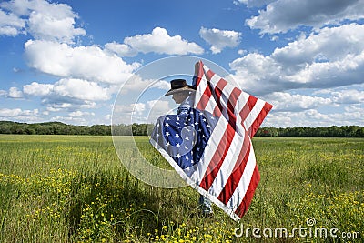 Man wearing cowboy hat running in beautiful grass field, American flag blowing in wind behind him Stock Photo