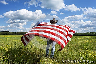 Man wearing cowboy hat standing in grass field, holding American flag blowing in wind behind him Stock Photo