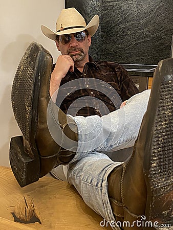 Man wearing cowboy straw hat and boots sitting down pondering, feet on the table Stock Photo