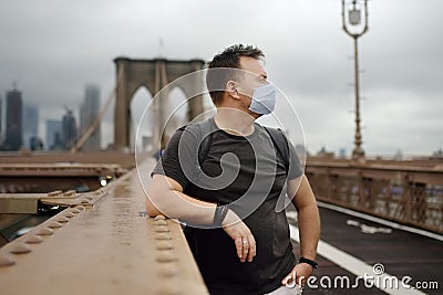Man wearing face mask on famous brooklyn bridge in rainy summer day. States lifting virus lockdown orders. Social distancing Stock Photo
