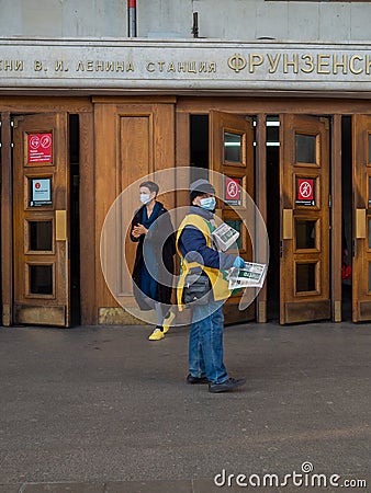 A man wearing a face mask and uniform distributes newspapers to people exiting the doors of a subway station Editorial Stock Photo