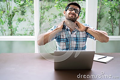 Man wearing glasses in casual clothes has a pain in the neck area while using a notebook computer to work at his home during the h Stock Photo