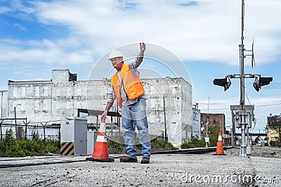 Man wearing hard hat and safety vest placing orange traffic cone pylon next to railroad tracks Stock Photo