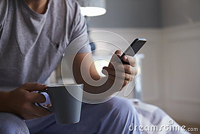 Man Wearing Pajamas Using Mobile Phone In Bedroom Stock Photo