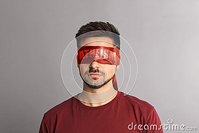 Man wearing red blindfold with word Atheism on light grey background Stock Photo