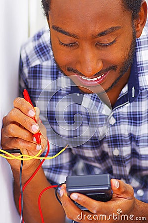 Man wearing white and blue shirt working on electrical wall socket wires using multimeter, electrician concept Stock Photo