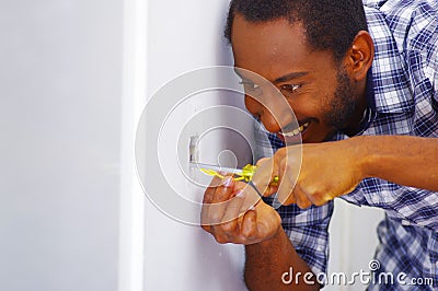 Man wearing white and blue shirt working on electrical wall socket wires using screwdriver, concentrated facial Stock Photo