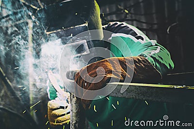 A man in weld mask with electric weld in his hand welding a metal frame Stock Photo