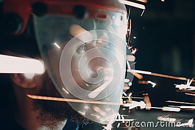 Man welder grinder in transparent protective mask with flying sparks in darkness. Stock Photo