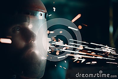 Man welder grinder in transparent protective mask with flying sparks in darkness. Stock Photo