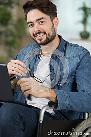 man in wheelchair using laptop and holding bankcard Stock Photo