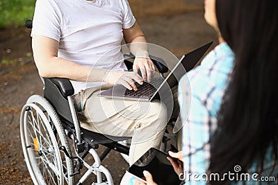 Man in wheelchair works on laptop on street next to woman sits and holds tablet Stock Photo