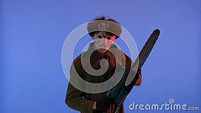 Man in white mask with chainsaw in hands on blue background with red neon light. Image of maniac Jason Voorhees from Stock Photo