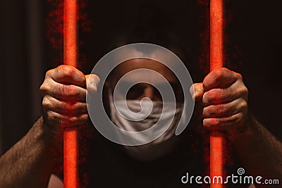 Man with white medical mask standing in the dark, holding red bars made of viruses with his bare hands, locked away in dark Stock Photo