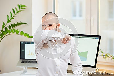 A man in a white shirt with a beard coughing in the bend of his elbow Stock Photo