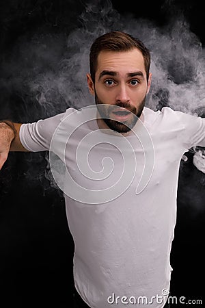 Man in white t-shirt on black background releasing a cloud of smoke Stock Photo