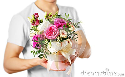 Man in white t shirt holding in hand rich gift bouquet. Composition of flowers in a pink hatbox. Tied with wide white ribbon and Stock Photo