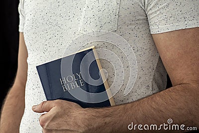 A man in a white T-shirt holds a bible in his hand. Stock Photo