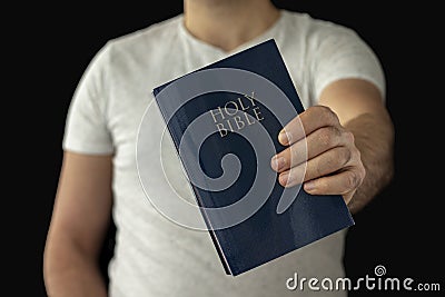 A man in a white T-shirt holds a bible in his hand. Stock Photo