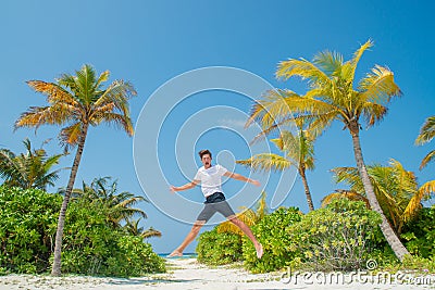 Man in white t-shirt jumping at the beach at the tropical island luxury resort Stock Photo