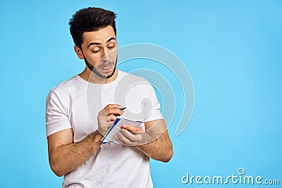 man in white t-shirt notebook with pen student blue background Stock Photo