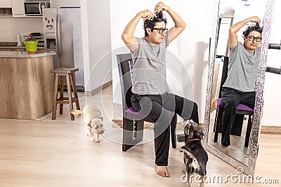 Man who is cutting his hair himself in front of a mirror in his living room with his dogs accompanying him Stock Photo