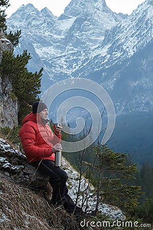 Man in winter mountains resting and drinking from vacuum flask metal cup Stock Photo