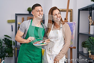 Man and woman artists smiling confident holding paintbrush and palette at art studio Stock Photo