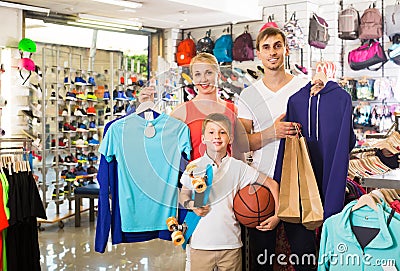man and woman with boy choosing t-shirts and other goods in sport shop Stock Photo