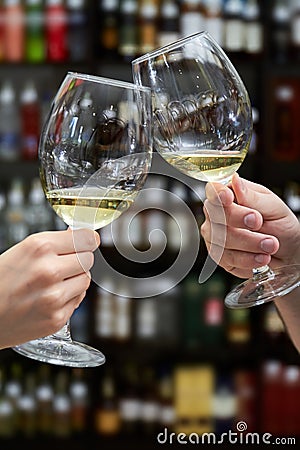 Man and woman clink glasses of white wine on the background of shelving with bottles of wine Stock Photo