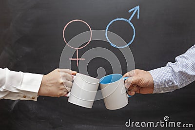 A man and a woman clink mugs against a background of gender symbols. Concept of gender equality Stock Photo