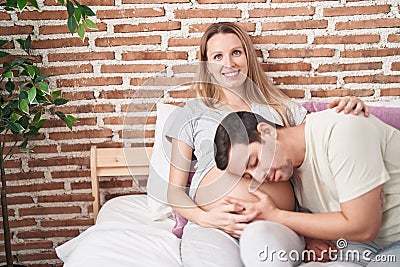 Man and woman couple listening baby sound sitting on bed at bedroom Stock Photo
