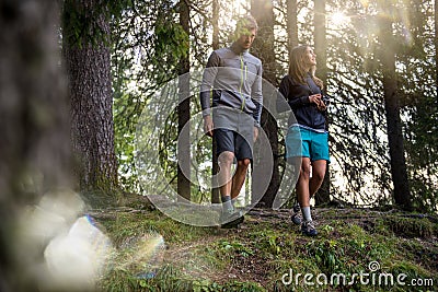 Man and woman couple walking in forest woods with sun flare light. Group of friends people summer adventure journey in Stock Photo