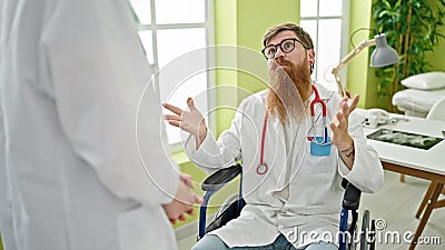 Man and woman doctors sitting on wheelchair speaking at clinic Stock Photo