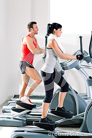 Man and woman with elliptical cross trainer at gym Stock Photo