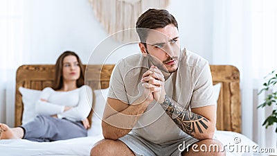 Man and woman feeling stressed and angry at each other, sits on wooden bed and look to side of free space Stock Photo